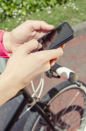 Closeup of beautiful young sportive woman with custom fixie bike looking her smartphone in a sunny summer day  Soft and warm tones の写真素材