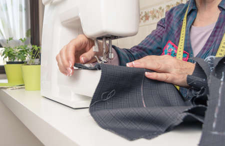 Senior seamstress woman working with clothing item on a sewing machineの写真素材