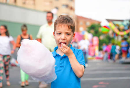 Portrait of cute child eating cotton candy over a summer fair festival backgroundの写真素材