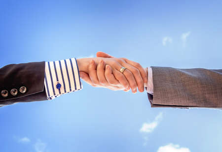 Closeup of a business handshake over blue sky backgroundの写真素材