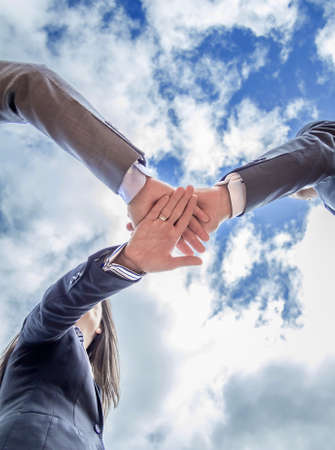 Bottom view of business team showing unity with hands together over blue sky backgroundの写真素材