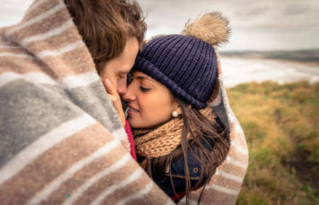Closeup of young beautiful couple embracing under blanket in a Day With Either cold and dark cloudy sky on the backgroundの写真素材