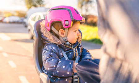 Portrait of little girl with security helmet on the head sitting in a bike seat behind of her father. Safe and child protection concept.の写真素材