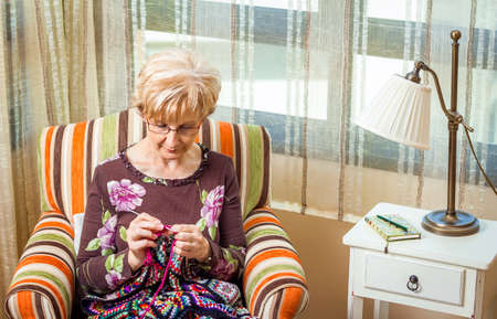 Portrait of senior woman knitting a vintage wool quilt with colorful patchesの写真素材