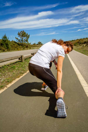 Back view of athletic young woman with sportswear suffering pain in her leg calf by a muscle cramp...