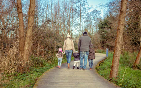Back view of family walking together holding hands over a wooden pathway into the forestの写真素材
