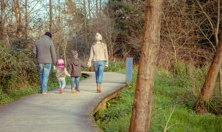 Back view of family walking together holding hands over a wooden pathway into the forestの写真素材