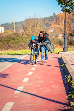 Mother teaching her son to ride a bicycles in the city on a sunny winter day.  Family leisure...