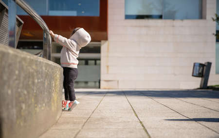Little girl with sneakers and hoodie training hard with a metal railing in a city squareの写真素材