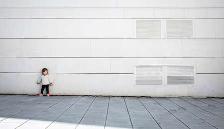 Little girl with sportive look posing in front of a modern white stone wallの写真素材