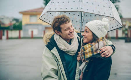 Portrait of young beautiful couple embracing and laughing under the umbrella in an autumn rainy day....