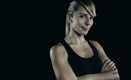 Portrait of beautiful athletic blonde woman posing with arms crossed over a dark backgroundの写真素材