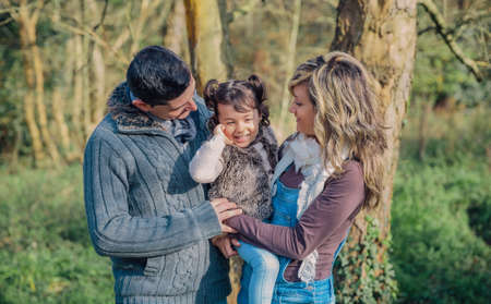 Portrait of happy couple with her little daughter enjoying together leisure over a forest background. Family time concept.の写真素材