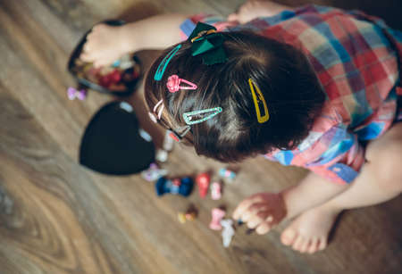Top view of cute baby girl head with a lot of hair clips playing sitting in a wooden floor at home. Selective focus on head.の写真素材