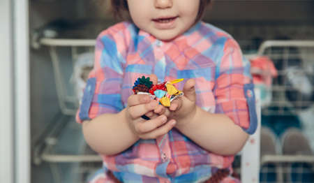 Closeup of cute baby girl playing with a lot of hair clips in her hands over a wooden floor at home. Selective focus on hair clips.の写真素材