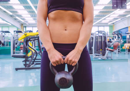 Closeup of beautiful woman with slim waist and black sportswear holding black iron kettlebell in a fitness centerの写真素材