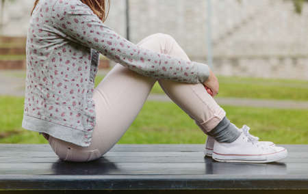 Closeup of beautiful young trendy woman sitting with her legs up on a park benchの写真素材