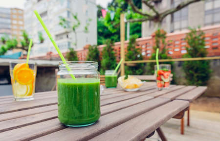 Green vegetable smoothies and infused fruit water cocktails over a wooden table outdoors. Healthy organic summer drinks concept.の写真素材