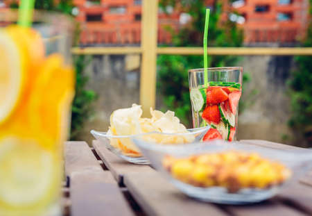 Infused fruit water cocktails and snacks bowls over a wooden table outdoors. Healthy organic summer drinks concept.の写真素材