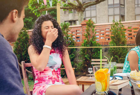 Beautiful young woman laughing with a friend around the table with healthy drinks in a leisure summer day outdoorsの写真素材