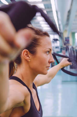 Closeup of beautiful woman doing hard suspension training with fitness straps in a fitness center. Healthy and sporty lifestyle concept.の写真素材