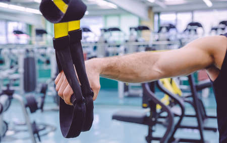 Closeup of fitness straps in the hand of man doing hard suspension training in a fitness center. Healthy and sporty lifestyle concept.の写真素材