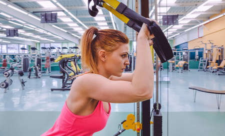 Portrait of beautiful woman doing hard suspension training with fitness straps in a fitness center. Healthy and sporty lifestyle concept.の写真素材