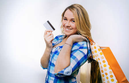Portrait of happy girl teenager showing a credit card and holding shopping bags. Young consumer...