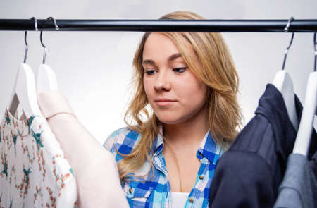 Portrait of doubtful girl teenager with blue plaid shirt looking different clothes indoors. Young consumer concept.の写真素材