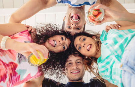 Below view of young happy people with their heads together and holding healthy drinks having fun in...