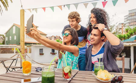 Group of young happy people taking a selfie with a electronic tablet in a summer party outdoors....