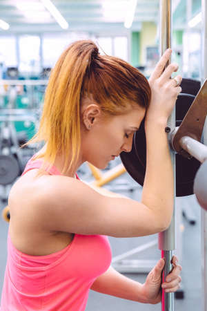 Beautiful sporty woman resting tired after lifting barbell on a muscular training in fitness center