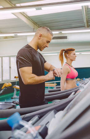 Portrait of handsome man checking heart rate on the watch during a hard treadmill training in fitness center. Sport and technology concept.の写真素材
