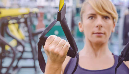 Closeup of fitness strap in the hand of woman doing hard suspension training in a fitness center. Healthy and sporty lifestyle concept.の写真素材