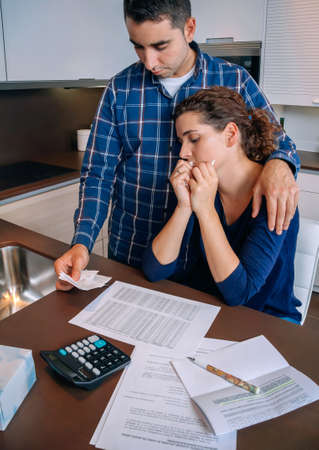 Young unemployed husband gives solace to his desperate wife crying by their debts. Financial family problems concept.の写真素材