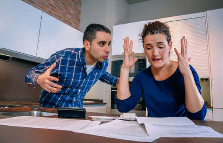 Angry young couple shouting in a hard quarrel by their many debts at home. Financial family problems concept.の写真素材
