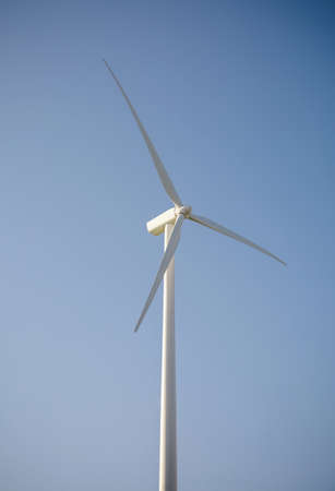 Closeup of windmill turbine and blades generating electricity over a blue sky background. Clean and ecological energy production concept.の写真素材