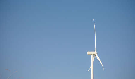 Closeup of windmill turbine and blades generating electricity over a blue sky background. Clean and...