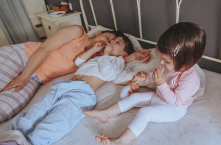 Portrait of happy children eating cookies in the bed with their mother in a relaxed morning. Weekend family leisure time concept.の写真素材