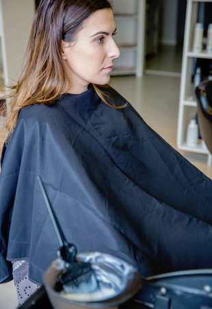 Beautiful young woman ready for a  hair color change with defocused hair dye in bowl and brush in the foregroundの写真素材