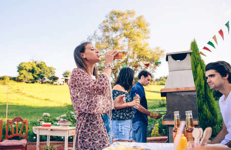 Young beautiful woman drinking bottle of beer in a outdoors summer barbecue with her friendsの写真素材