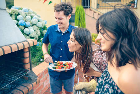 Group of young friends cooking vegetable skewers and having fun in a outdoors summer barbecueの写真素材
