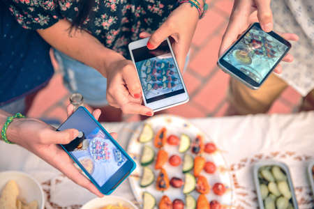 Closeup of young friends hands taking photos with their smartphones to vegetable skewers over a table in a outdoors summer barbecueの写真素材