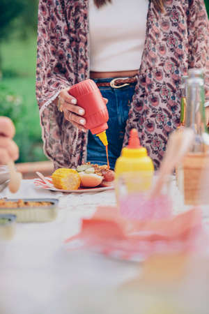 Closeup of woman hand pouring ketchup over an american hot dog in a outdoors summer barbecueの写真素材
