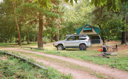 Landscape of 4x4 offroad vehicle with tent in the roof ready for camping next to dirt road with the forest in the backgroundの写真素材