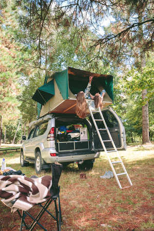 Young women friends resting lying on her back in a tent on the roof of 4x4 vehicle and looking the...