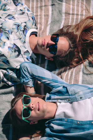 View from above of two beautiful young women with sunglasses lying in a striped blanket taking a sunbath. Relax and leisure time concept.の写真素材