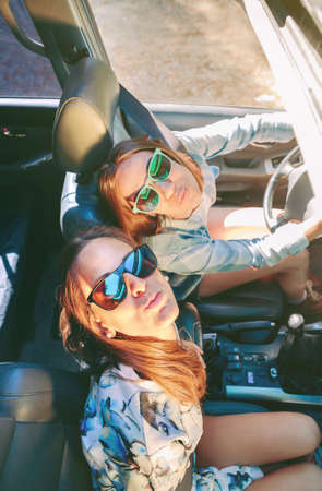 Top view of happy young women friends with sunglasses having fun inside of cabriolet car in a road...