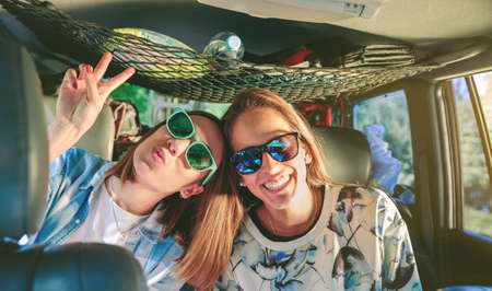 Two happy young women friends with sunglasses laughing and having fun inside of car in a road trip adventure. Female friendship and leisure time concept.の写真素材