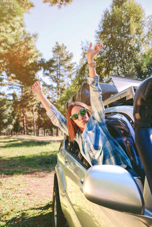 Portrait of happy young woman raising her arms through the window car in a sunny day over a nature background.の写真素材